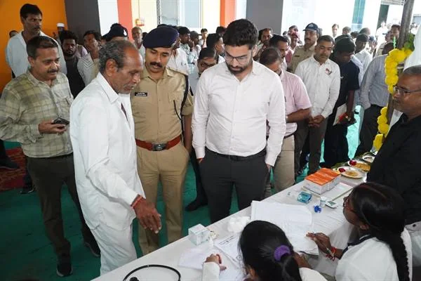 एक कार्यक्रम में सफेद शर्ट पहने अधिकारी और पुलिसकर्मी मेज पर बैठी महिला कर्मचारियों से जानकारी लेते हुए